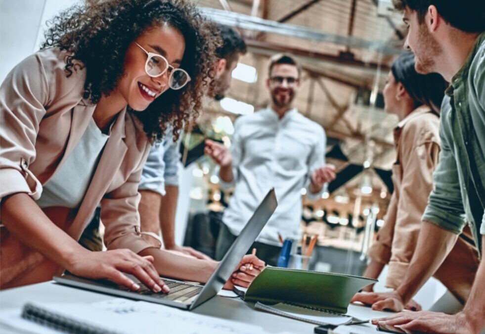 Diverse marketing and sales team collaborating around a laptop in a modern office, illustrating business alignment and strategy planning.