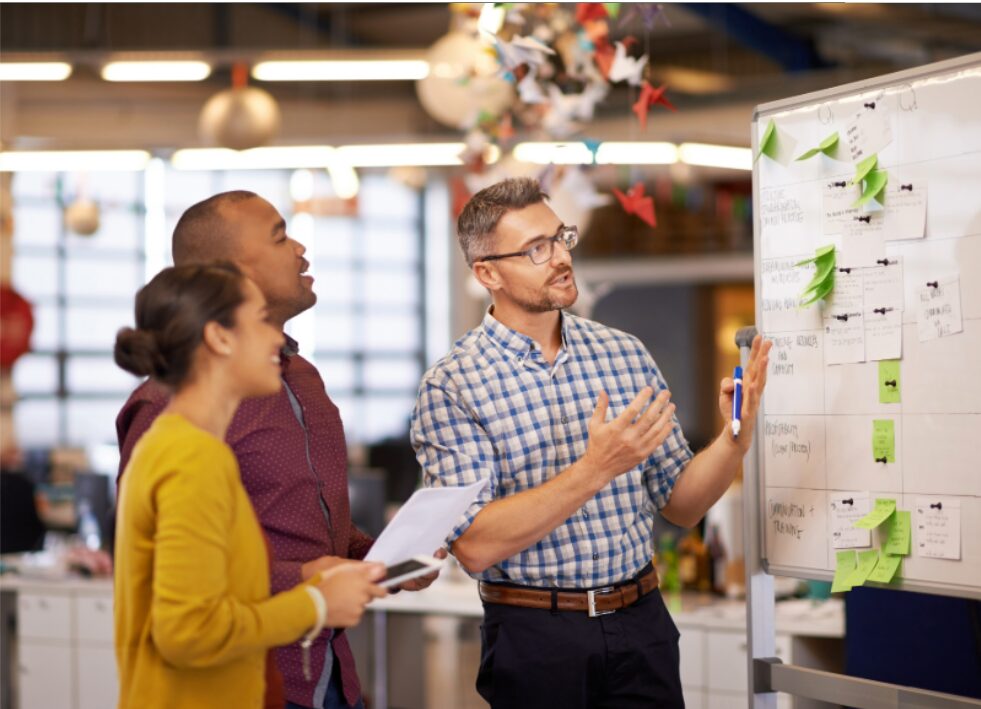 Marketing team collaborating at a whiteboard covered in notes, representing marketing operations turning strategic plans into actionable systems.
