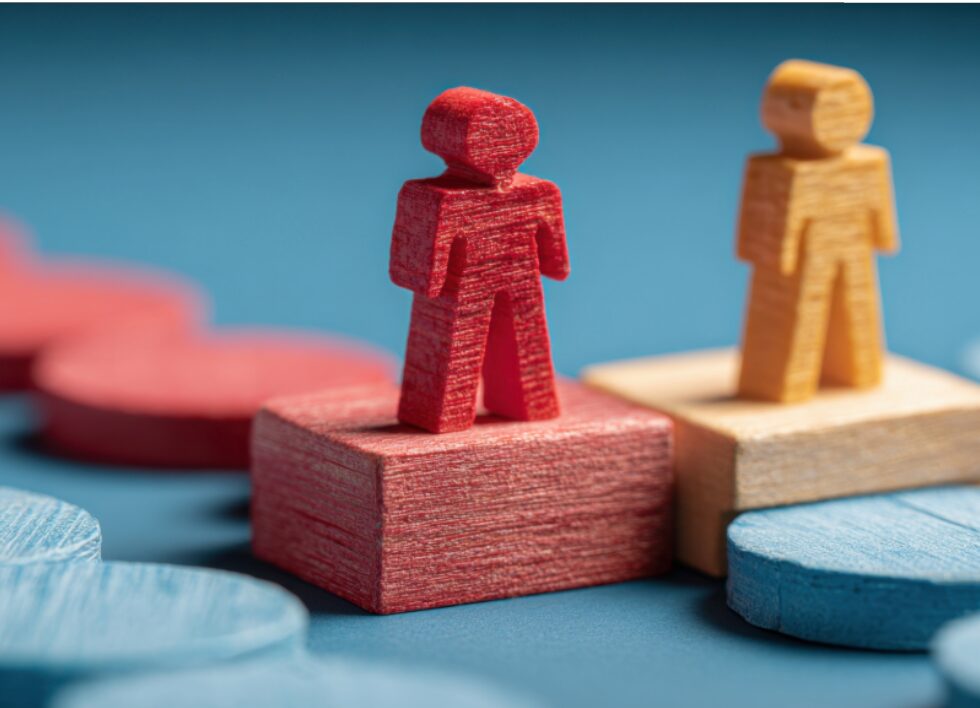 Concept image symbolizing marketing and sales alignment. Red and yellow wooden figures standing on adjacent blocks, representing teamwork and shared goals.